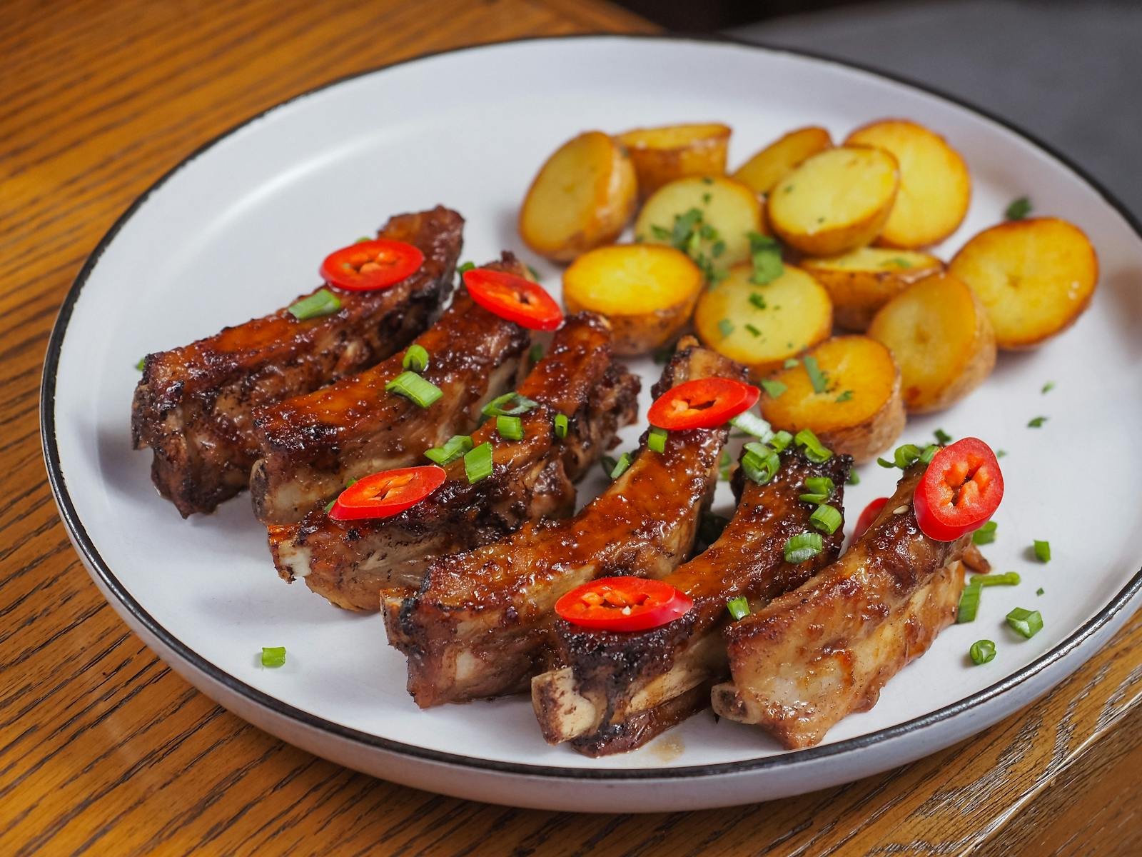 Close-up of spicy barbecue ribs with crispy roasted potatoes on a plate.