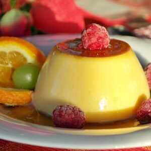 Indulge in creamy flan topped with raspberries, paired with citrus and caramel sauce for a delightful dessert treat.
